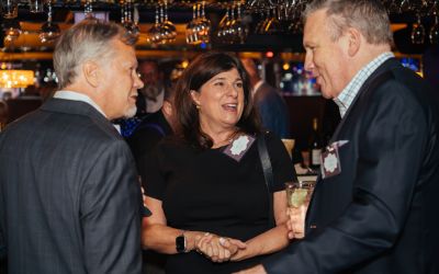 A woman and two men converse and laugh at the Professional Advisors dinner